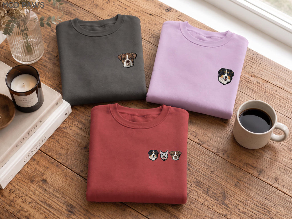 May include: Three crewneck sweatshirts in charcoal gray, light purple, and brick red. The charcoal sweatshirt features a single embroidered dog face, the purple one has a different dog face, and the red one displays three small embroidered dog faces.