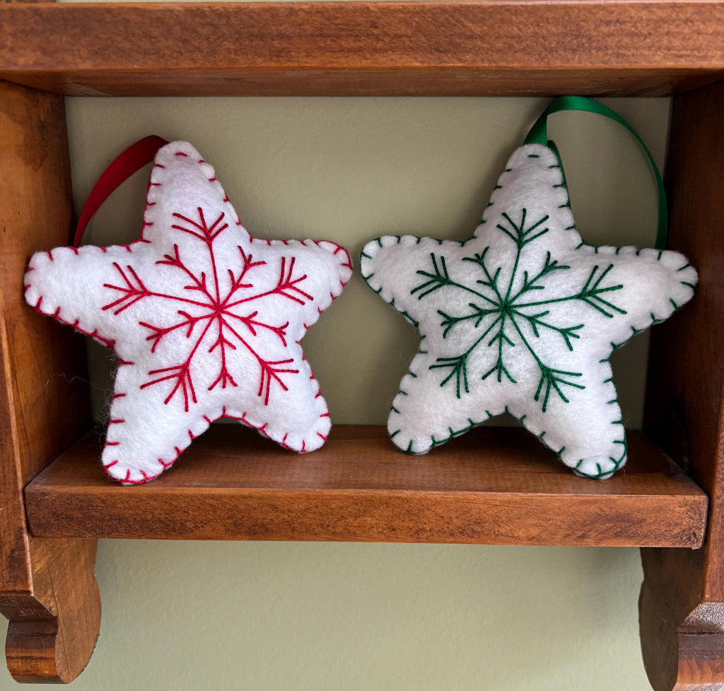 May include: Two white felt star ornaments with embroidered snowflakes. One snowflake is red and the other is green.