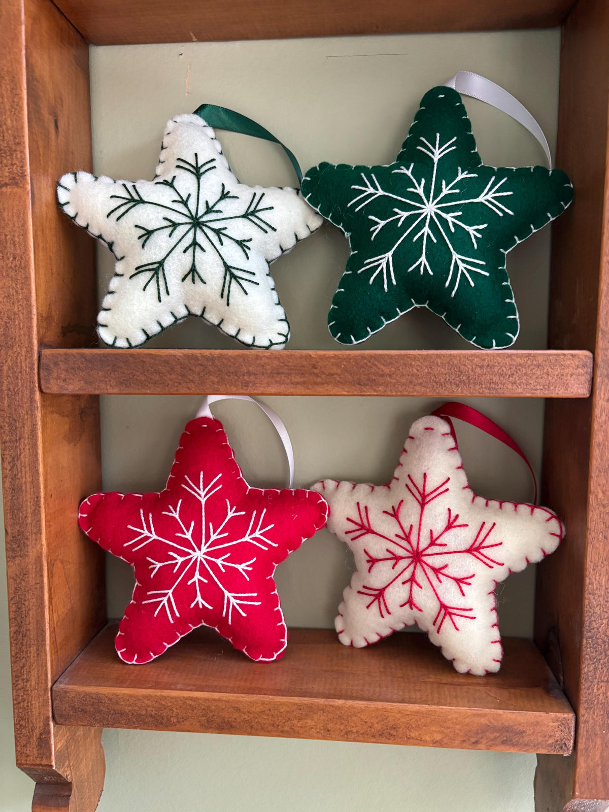 May include: Four felt star ornaments with embroidered snowflakes. Two stars are white with green snowflakes, and two stars are red with white snowflakes.
