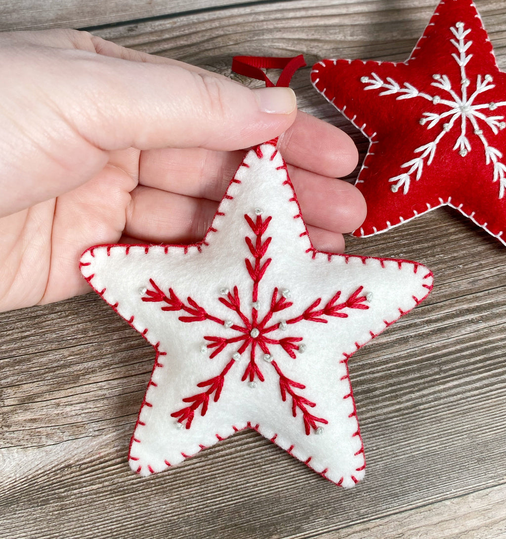 May include: Two felt star ornaments with red and white snowflake embroidery. The stars are white with red stitching and the snowflakes are red with white stitching.