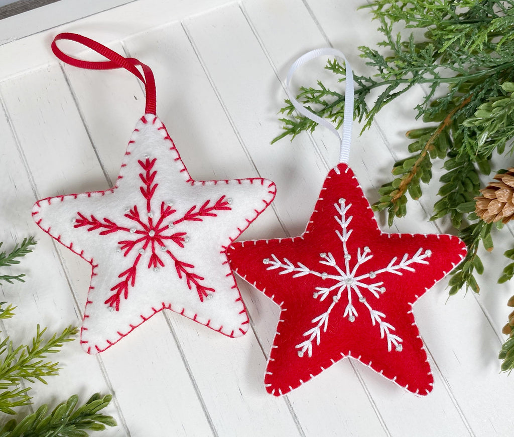 May include: Two felt star ornaments with white snowflake embroidery and white bead accents. One star is red and the other is white.