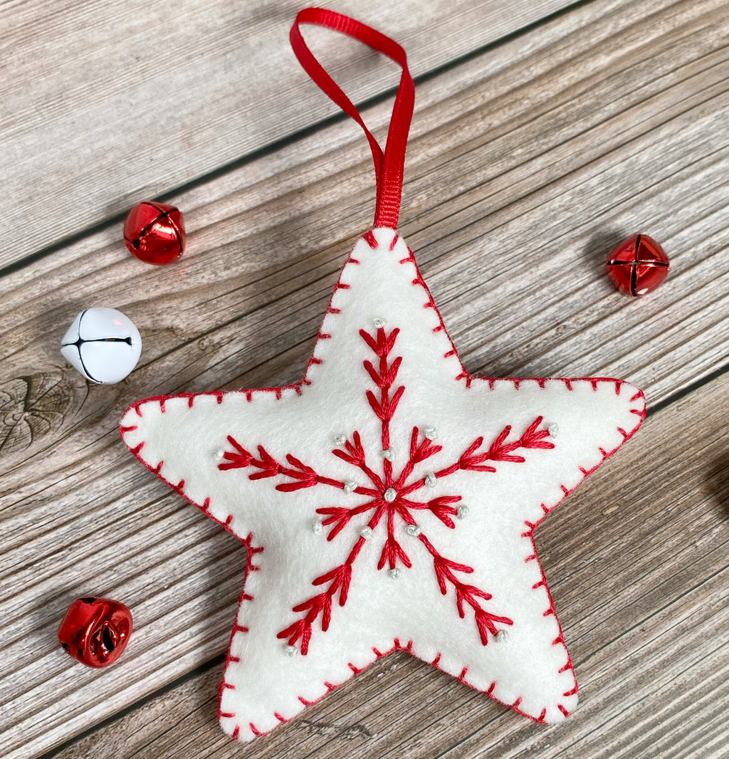May include: White felt star ornament with a red embroidered snowflake design and a red ribbon for hanging.