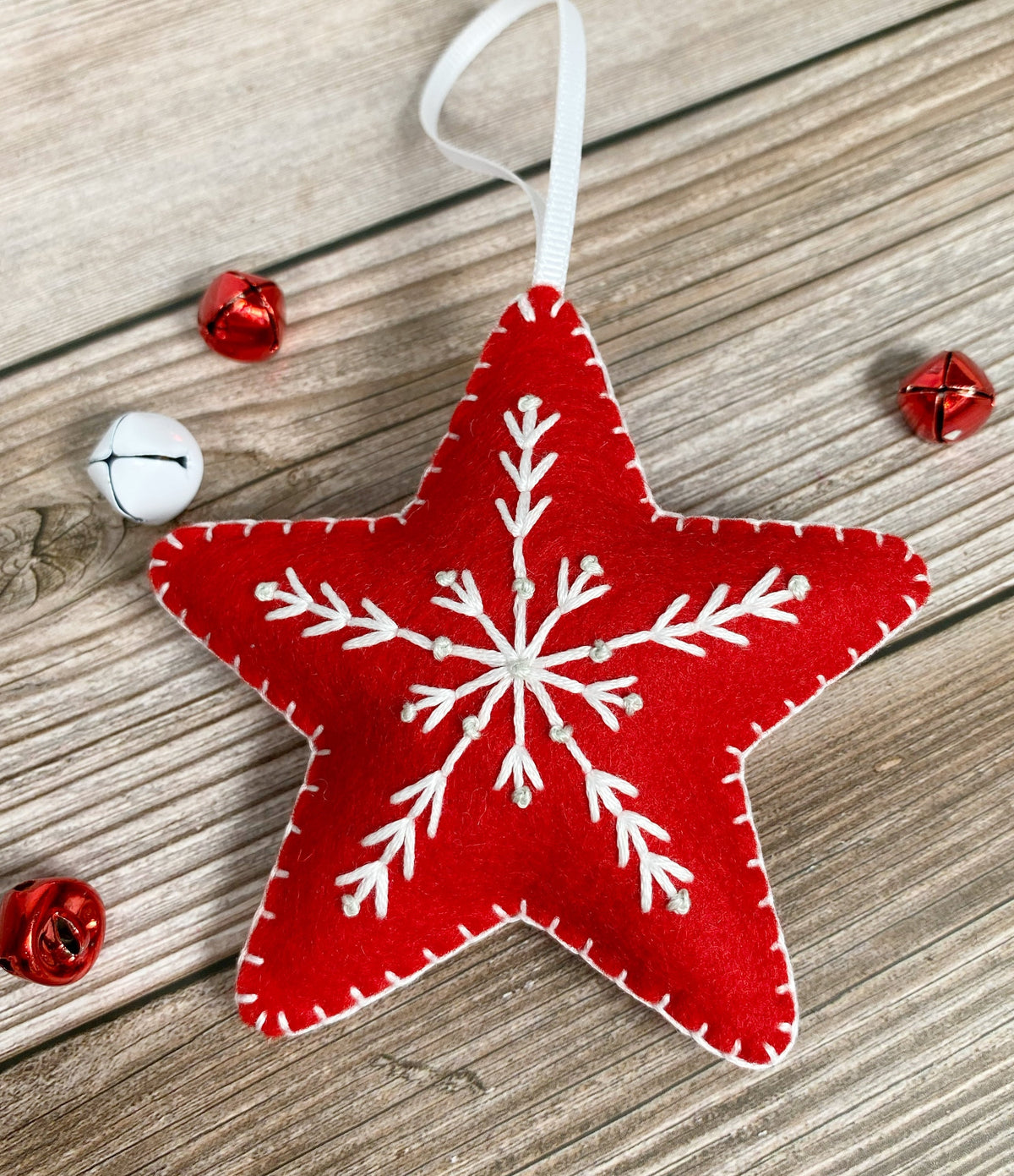 May include: Red felt star ornament with a white embroidered snowflake design. The star has a white ribbon loop for hanging.