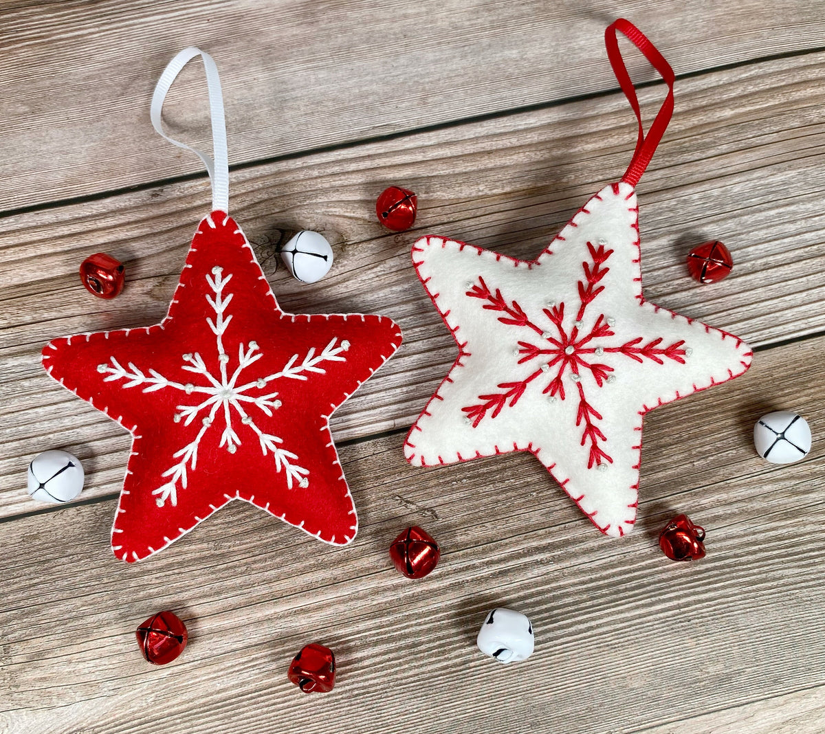 May include: Two felt star ornaments with snowflake designs. One star is red with white snowflakes, and the other is white with red snowflakes. The stars are surrounded by small jingle bells.