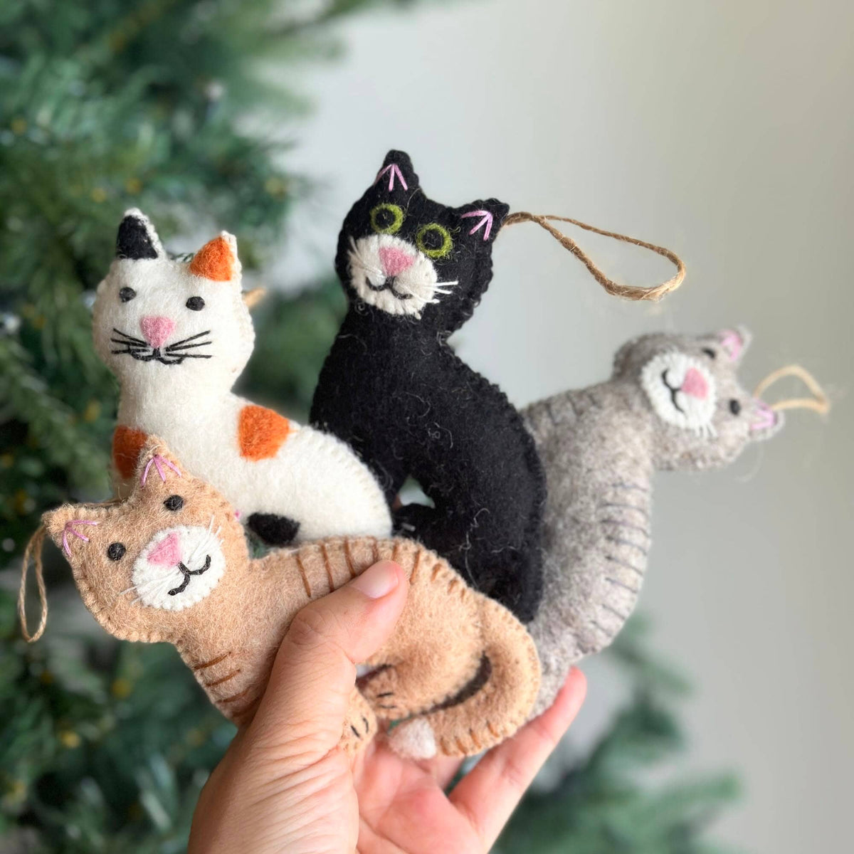 May include: Four felt cat ornaments in different colors and patterns. The cats are all smiling and have embroidered details. The ornaments are perfect for adding a touch of whimsy to your Christmas tree.