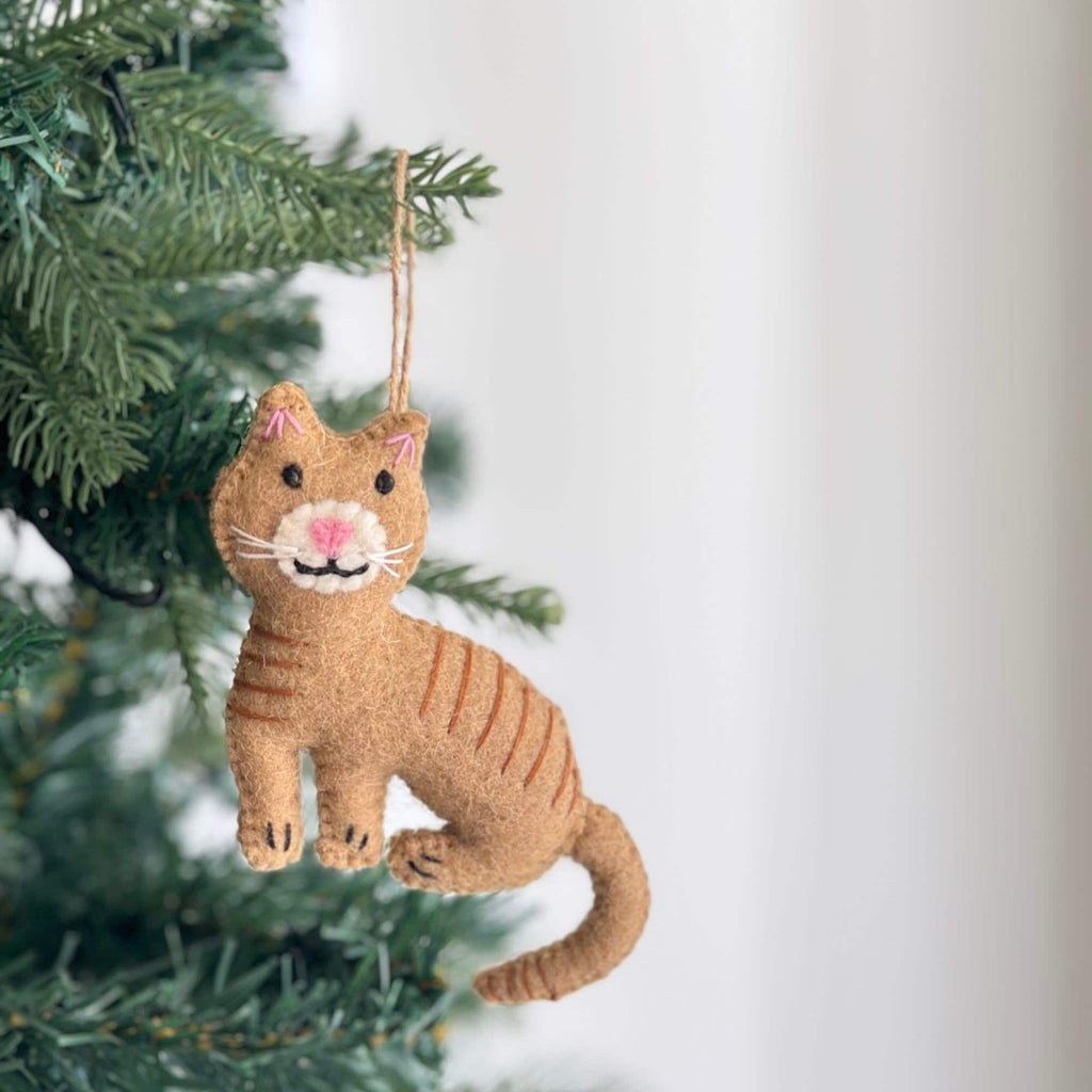May include: A felt orange tabby cat ornament with pink ears and a white face. The cat is hanging from a tree branch.