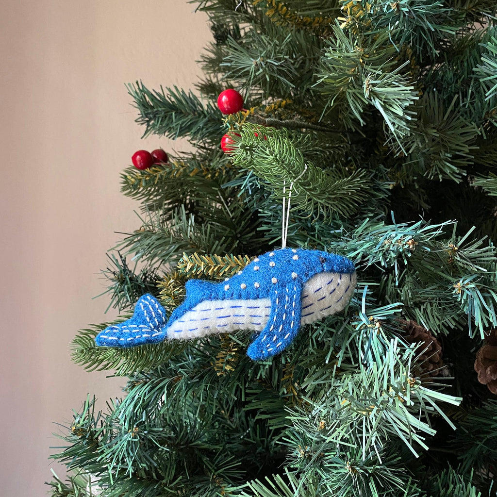 May include: A blue felt whale ornament with white stitching and white polka dots hanging on a green Christmas tree.