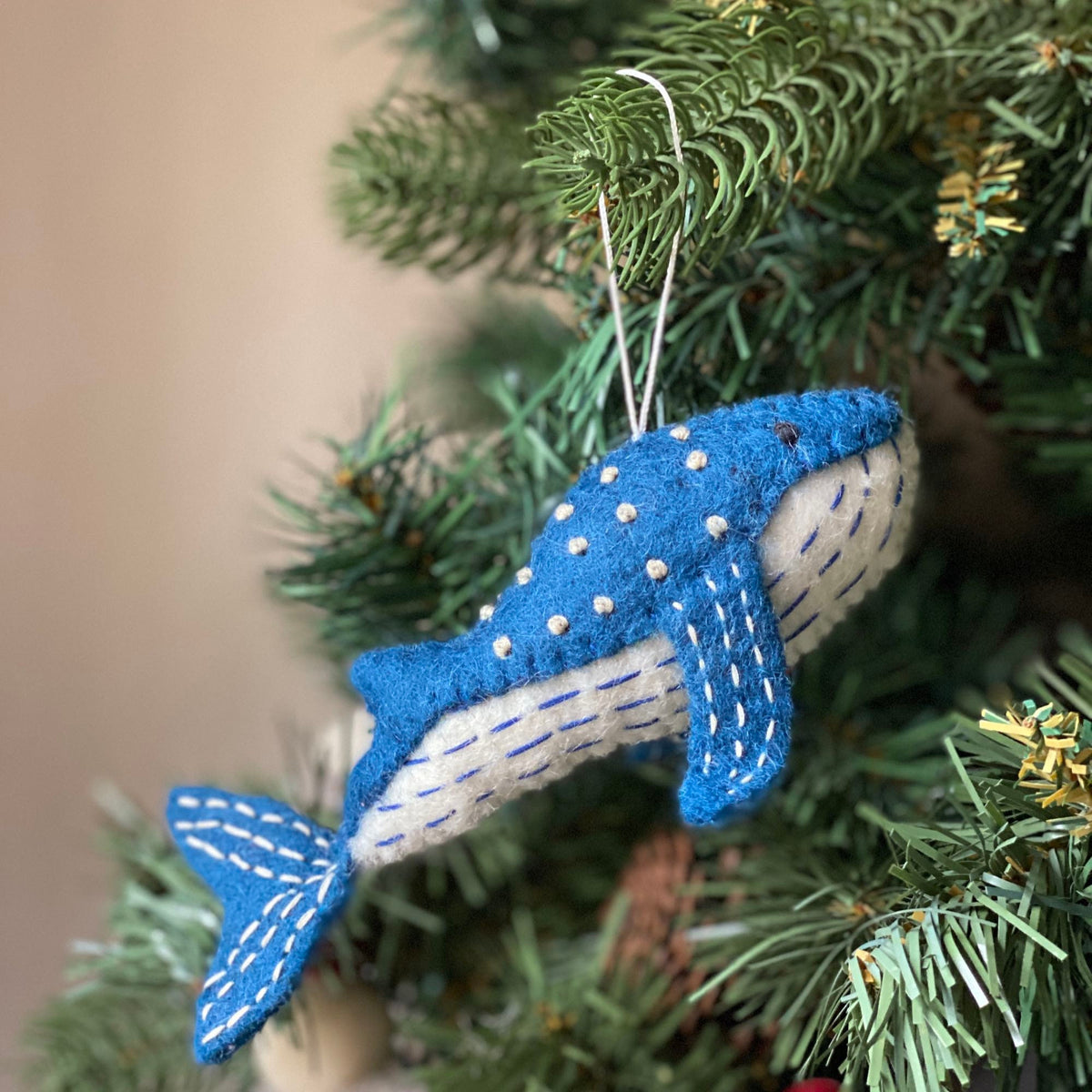 May include: A blue felt whale ornament with white stitching and white dots. The whale is hanging from a white string.